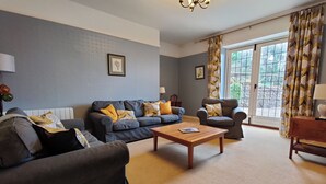 A living room with a sofa, armchair, coffee table, and a view through a window. - bossington bunkhouse (Bossington)