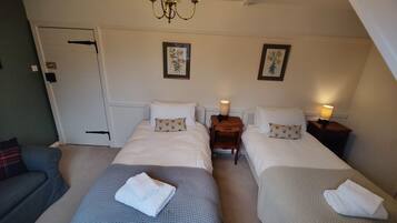 A twin room with two beds, a chandelier, a door, and framed pictures on the wall.