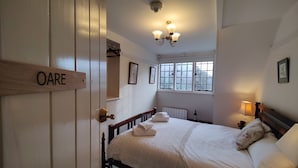 A bedroom with a bed, a bedside table, a lamp, a window, and a door labeled "OARE". - bossington bunkhouse (Bossington)