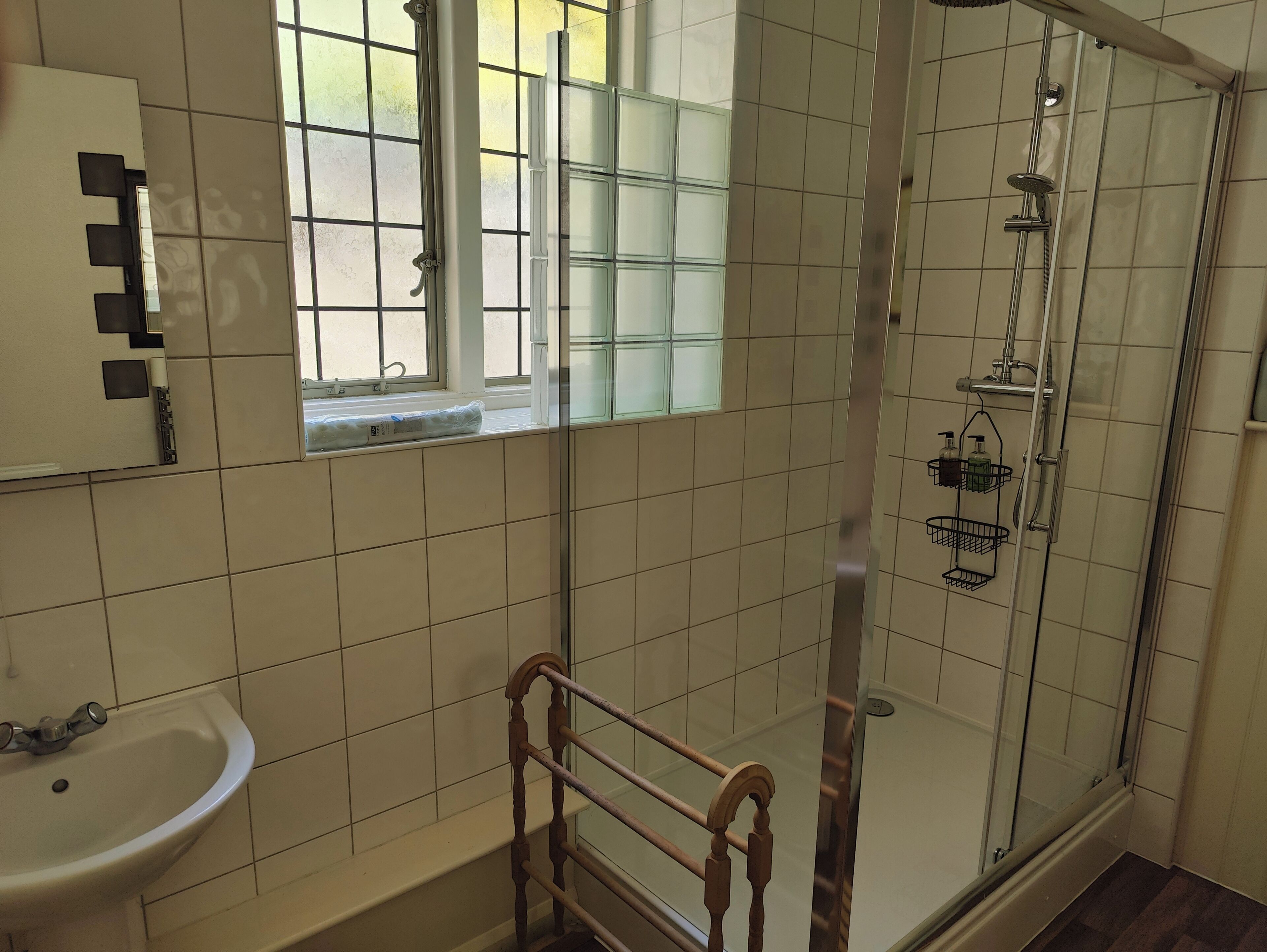 A bathroom with a glass-enclosed shower, a sink, a window, and a mirror.