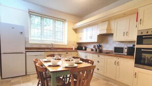 A kitchen with white cabinets, a dining table set with bowls and glasses, a refrigerator, and a microwave. - bossington bunkhouse (Bossington)
