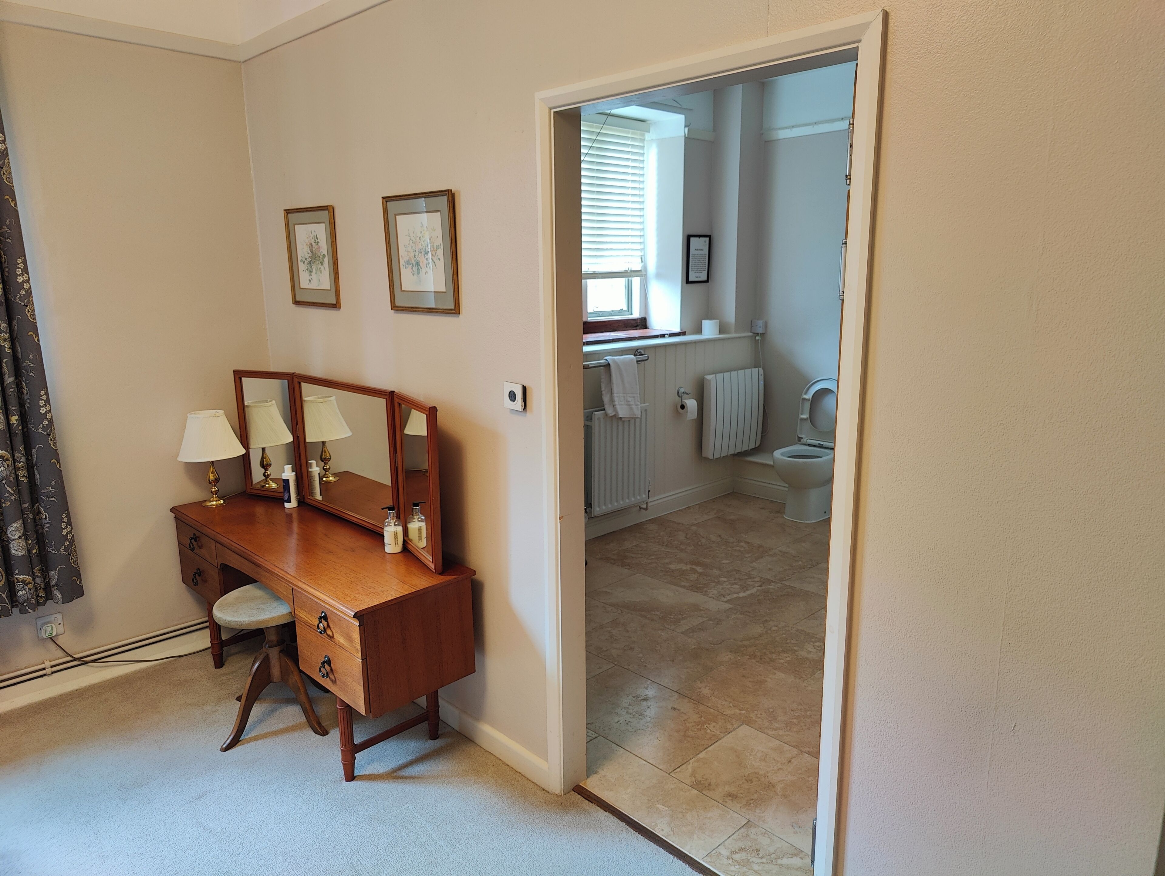 Een slaapkamer met een houten dressoir, twee spiegels en een raam.