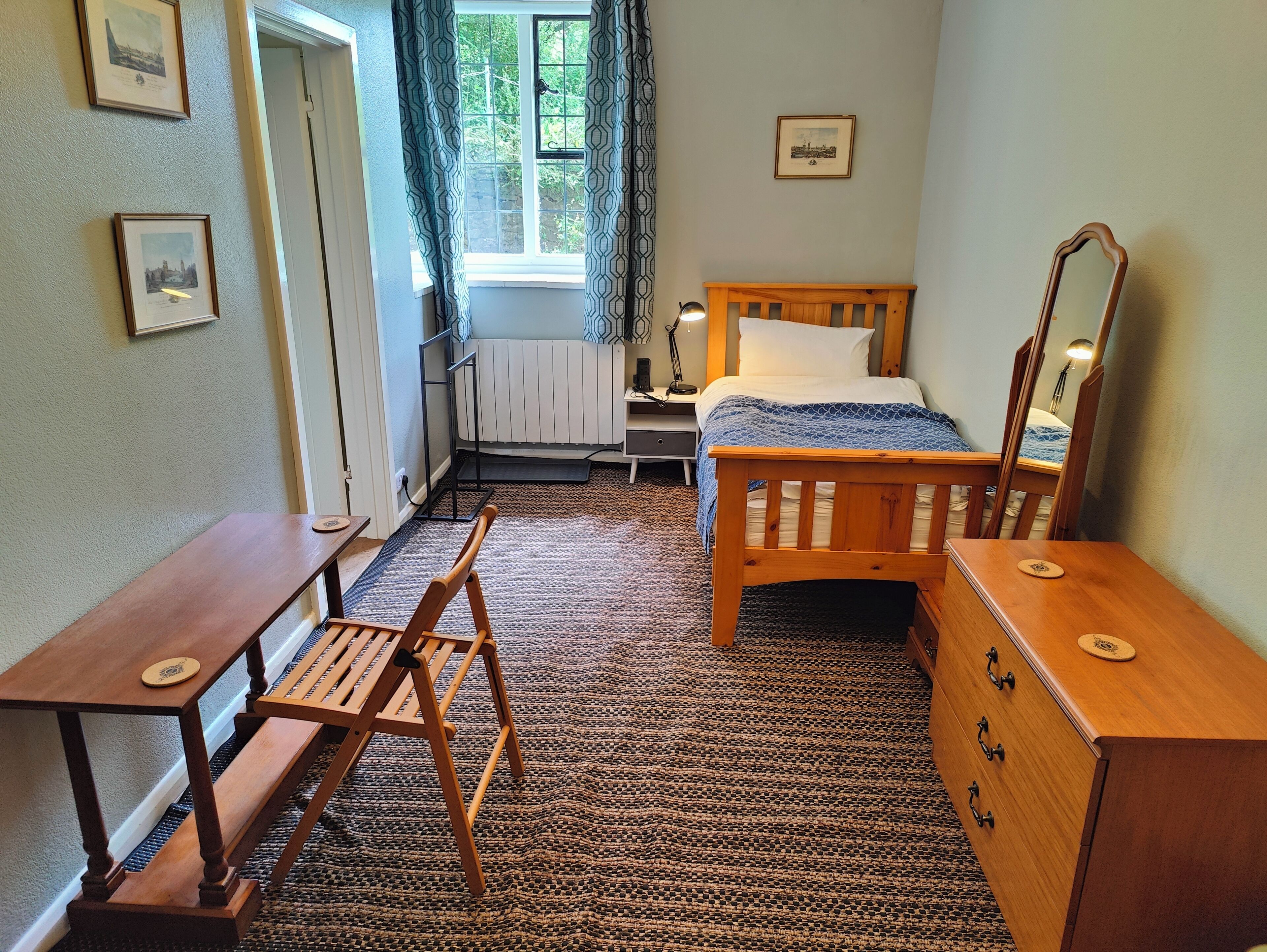 Une pièce comprenant un lit, un bureau, une chaise, une commode, un radiateur et une fenêtre avec des rideaux.