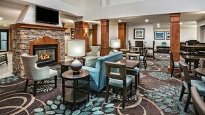 A hotel lobby with a stone fireplace, comfortable seating, a flat-screen TV, and a patterned carpet.
