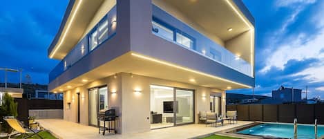 Una casa moderna de dos pisos con un porche cubierto, piscina y césped bien cuidado.