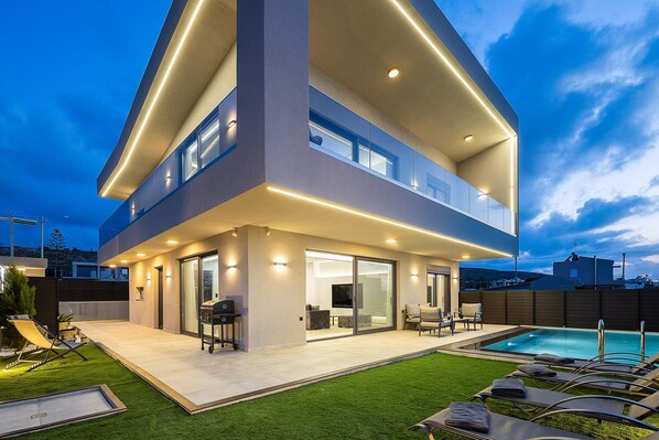 A modern two-story house with a covered patio, a swimming pool, and a well-maintained lawn.