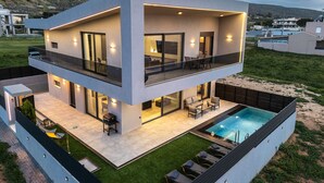 A modern two-story house with a balcony, a swimming pool, and a view of the surrounding landscape.