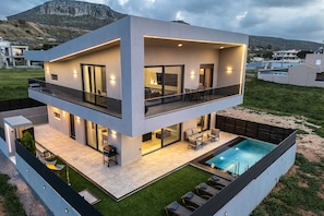 A modern two-story house with a balcony, a swimming pool, and a view of the surrounding landscape.