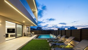 A modern outdoor living area with a pool, lounge chairs, and a flat-screen TV.