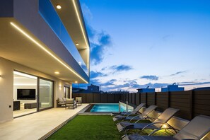 A modern outdoor living area with a pool, lounge chairs, and a flat-screen TV.