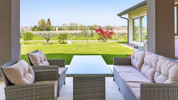 A patio with wicker furniture, a table, and a view of a vineyard. - Regarda - Lagobaldo Apartment with pool and garden (Lazise)