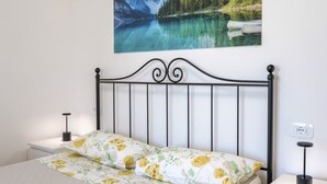 A neatly made bed with floral bedding, a wall-mounted picture of a lake, and bedside lamps. - Regarda - Lagobaldo Apartment with pool and garden (Lazise)