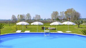 A swimming pool with white umbrellas and lounge chairs, surrounded by a grassy area and trees. - Regarda - Lagobaldo Apartment with pool and garden (Lazise)