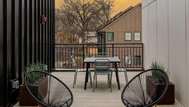 A modern outdoor patio with a table and chairs, string lights, and a view of buildings in the background. - The Lyric Loft - Walkable & Close to Downtown (Nashville)