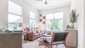 A spacious living room with a leather sofa, a grey armchair, a wooden chair, a round coffee table, and a rug. - The Lyric Loft - Walkable & Close to Downtown (Nashville)