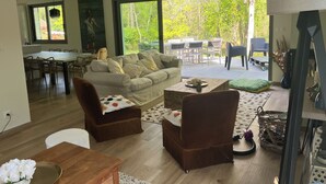 A spacious living area with a large sofa, two armchairs, a coffee table, and a dining table with chairs. There is a large window providing a view of the outdoors. - Pretty villa in the forest of Le Touquet Ideal family vacation ❤️classé 4*! (le touquet)