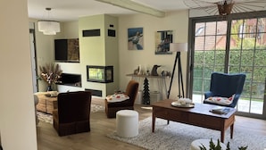 A modern living room with a sofa, armchair, and coffee table, a television, and a large window with a view of greenery. - Pretty villa in the forest of Le Touquet Ideal family vacation ❤️classé 4*! (le touquet)