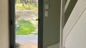 A view through a glass door into a green outdoor area with trees and a lawn. - Pretty villa in the forest of Le Touquet Ideal family vacation ❤️classé 4*! (le touquet)