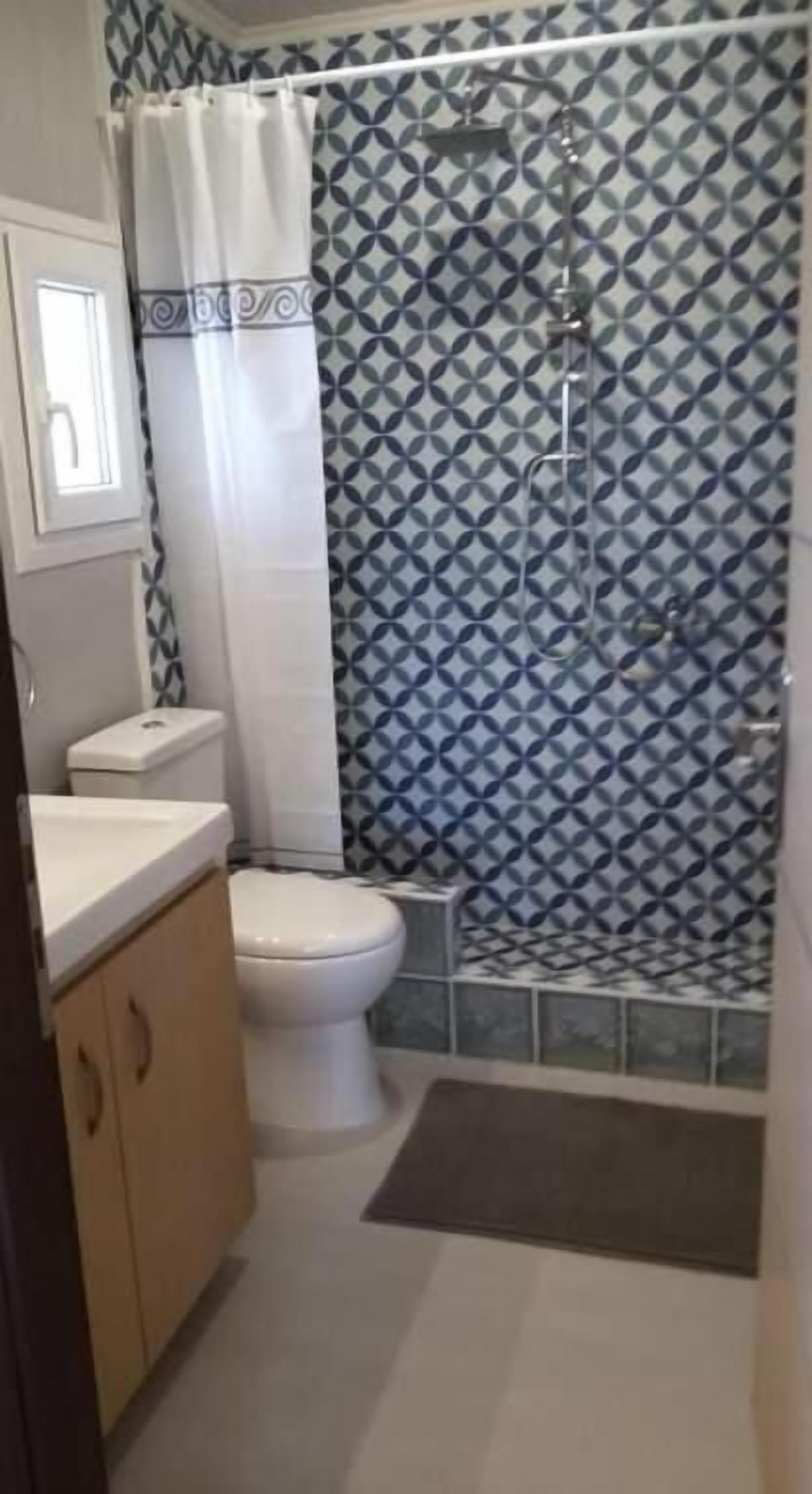 Een badkamer met een toilet, een douche met een behang en een raam.
