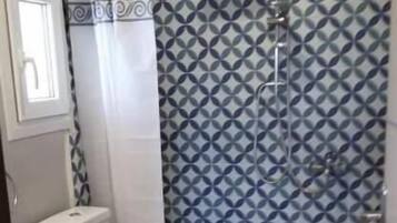 Een badkamer met een toilet, een douche met een behang en een raam.