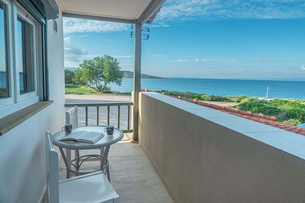 A balcony with a table and chairs, overlooking a coastal view with a clear sky.