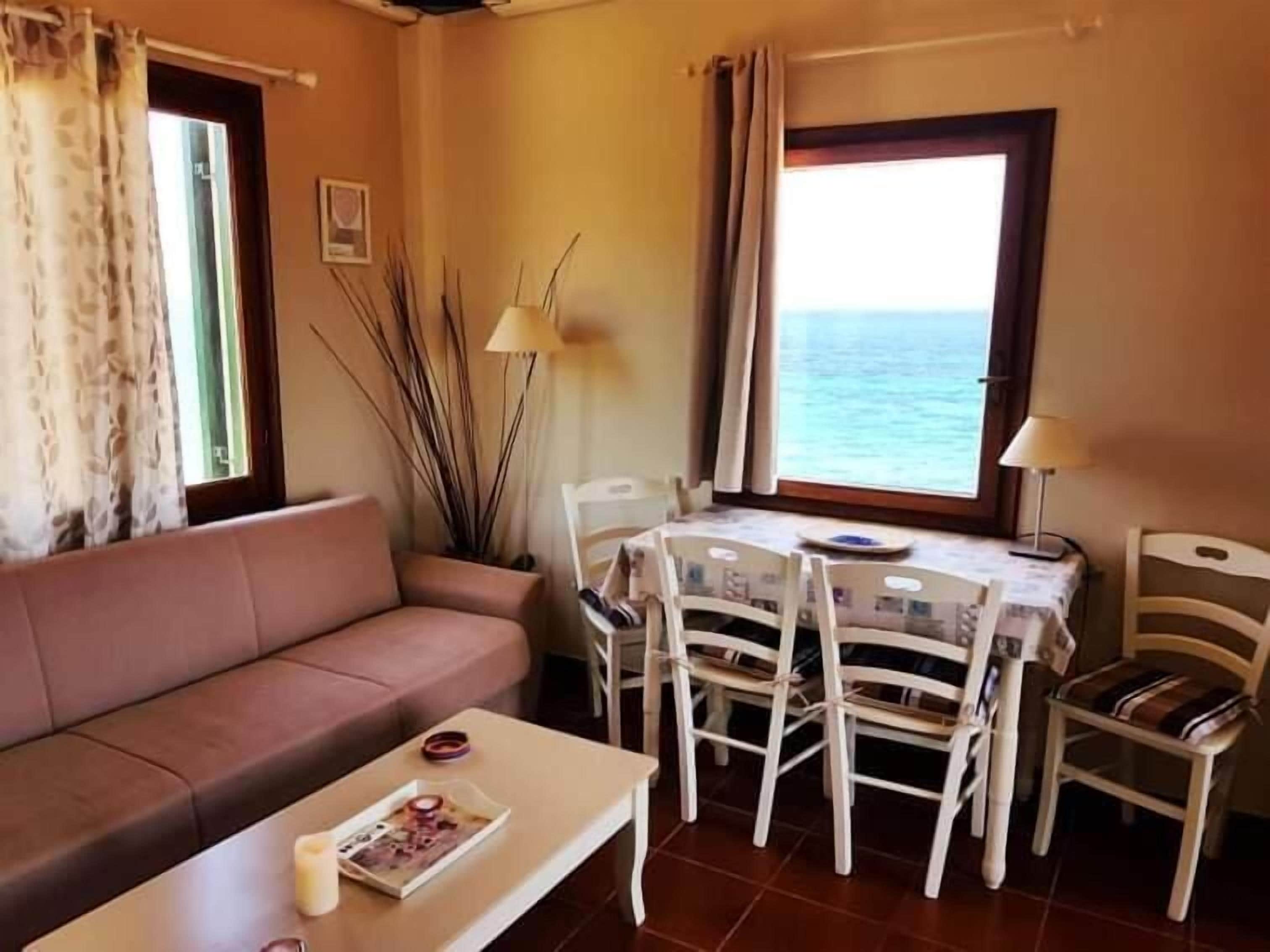 Een gezellige zithoek met een bank, een klein tafeltje met een tijdschrift en een eettafel met stoelen. Er is een raam met uitzicht op zee.