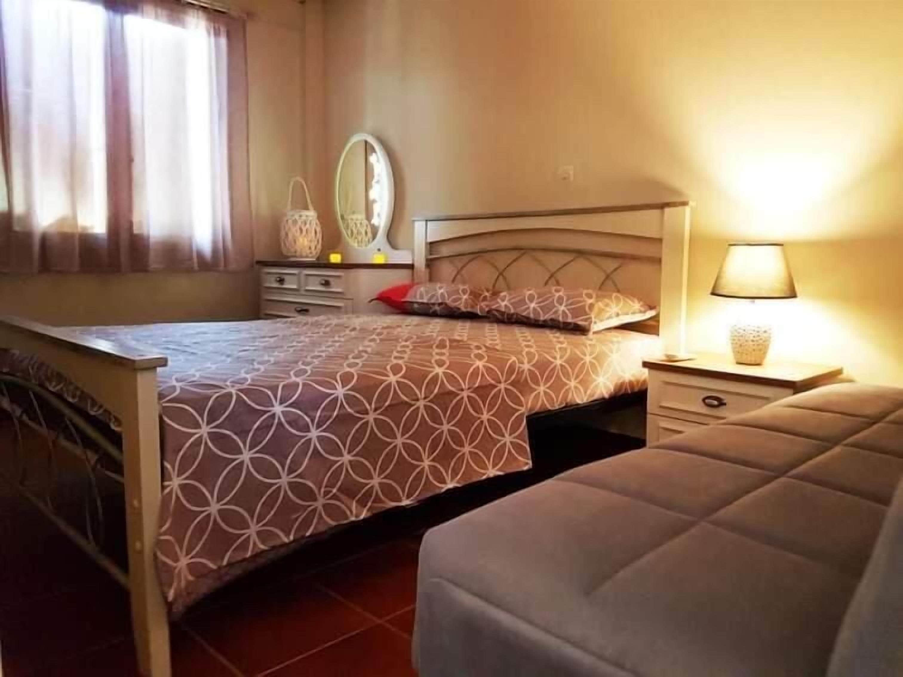 Quarto com cama, mesas de cabeceira, espelho e janela com cortinas.
