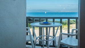 A balcony with a table and chairs overlooking a beach with a sailboat in the distance. - Aegean Bliss Residences Karfas (Chios)
