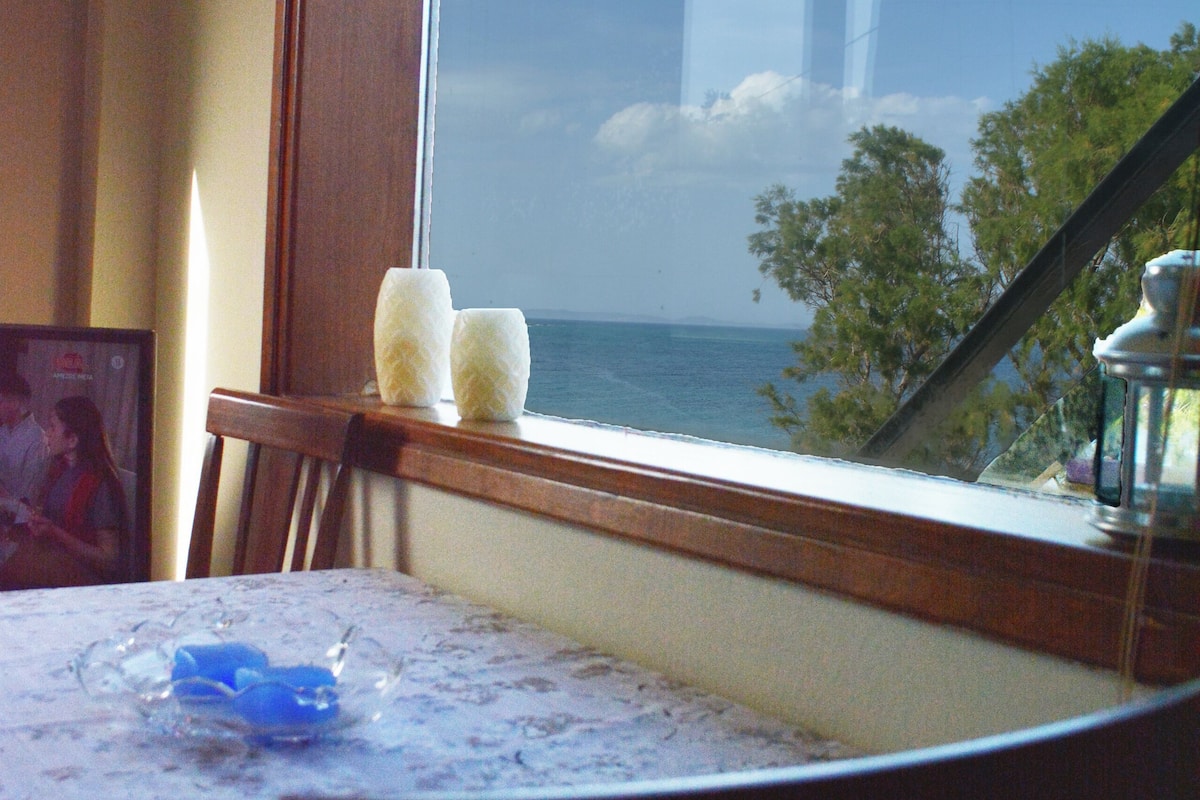 A table with a view of the ocean through a window, a picture frame, and two candles on the windowsill.