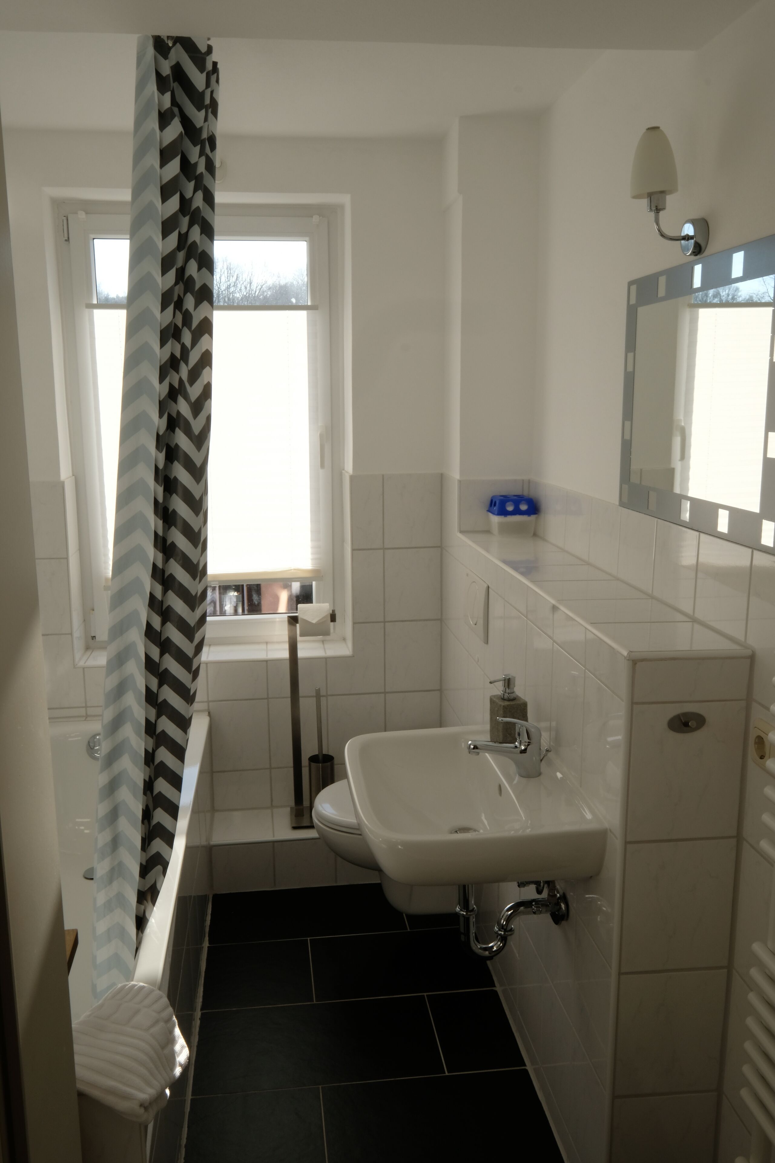 A bathroom with a white sink, a mirror, and a window with a black and white chevron curtain.
