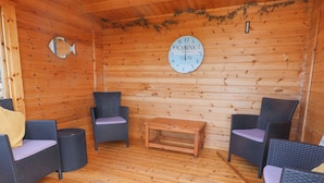 Interior de una cabaña de madera con sillones de mimbre, una mesa de madera y una decoración con forma de pez en la pared.