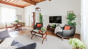 Un salon spacieux doté d’un plafond en bois, d’un téléviseur à écran plat, de sièges confortables et d’un coin repas avec une table et des chaises.