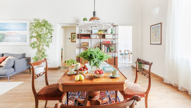 Un coin repas avec une table en bois, des chaises, un luminaire suspendu et une bibliothèque remplie de livres et de plantes.
