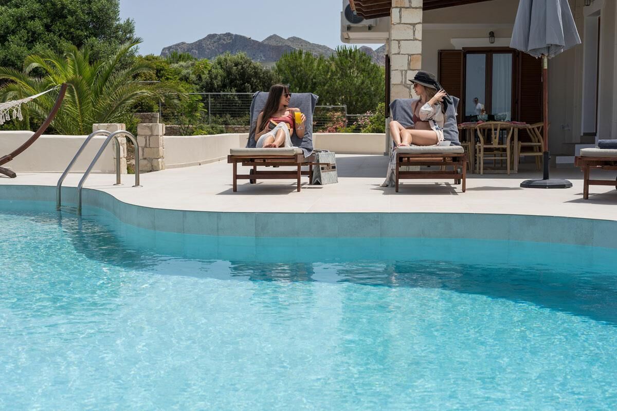 A pool area with two lounge chairs and a table, surrounded by a stone wall and greenery.