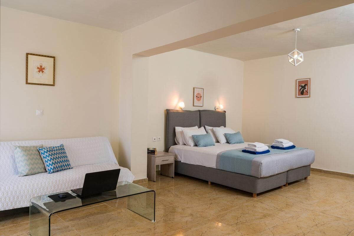 A modern hotel room with a bed, a sofa, a glass coffee table, and a nightstand.