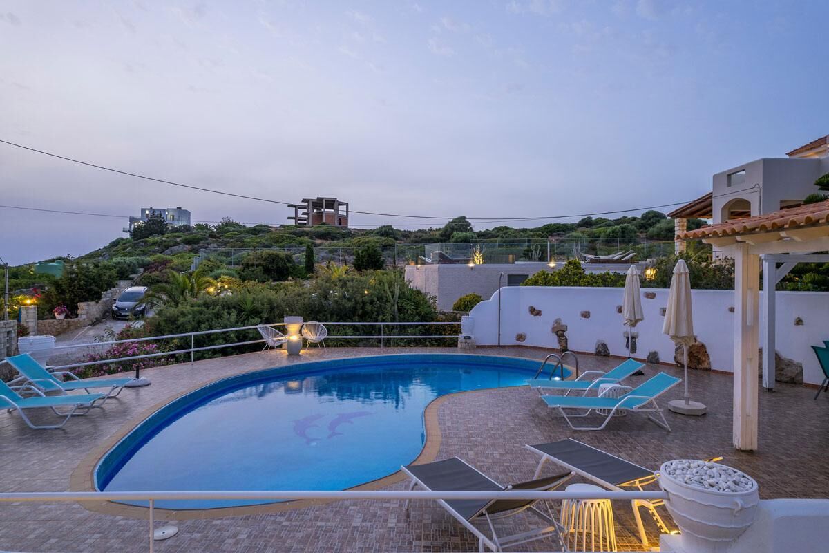 A swimming pool with lounge chairs and umbrellas, surrounded by a landscaped garden and a view of a hill with buildings.