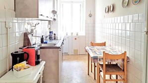 Une cuisine compacte avec des carreaux blancs, une machine à café, un évier et une table à manger avec des chaises.