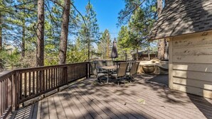 A wooden deck with outdoor furniture, surrounded by tall trees.