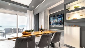 A modern dining area with a wooden table, grey chairs, and a TV mounted on the wall.