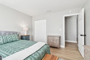 Une chambre à coucher comprenant un lit, une table de chevet, une commode et une porte ouverte donnant sur une autre pièce.