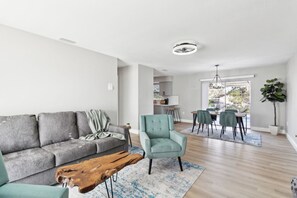 A modern living room with a sofa, armchair, coffee table, and dining area with chairs and a table.