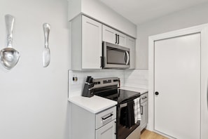 A compact kitchen with white cabinetry, a microwave, a stove, and a door.
