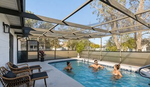 Une piscine extérieure dotée d’un espace couvert, entourée de chaises et de plantes en pot.