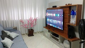 Una sala de estar con un televisor sobre un mueble de madera, una planta en maceta y una cama con almohadas.