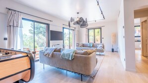 A spacious living area with a sofa, a coffee table, and a television. There are large windows providing natural light and a view of the outdoors. - Wonderful Villa, swimming pool and parking (Nice)