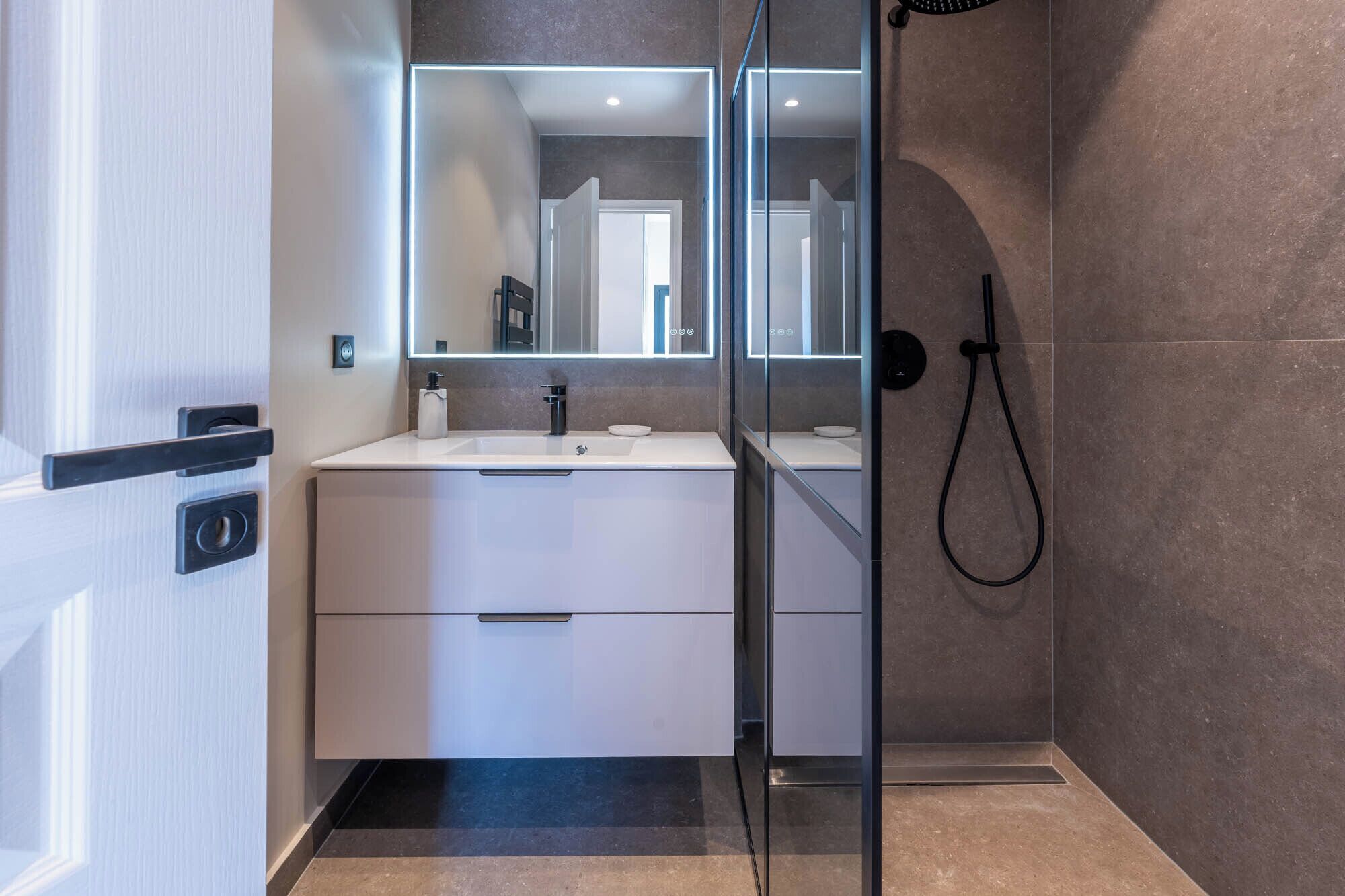 A modern bathroom with a glass-enclosed shower, a white vanity with a mirror, and a black shower hose.