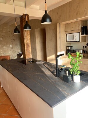 A modern kitchen with a marble countertop, black pendant lights, a sink, and a microwave.