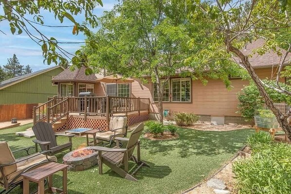 A backyard with a wooden deck, outdoor furniture, and a fire pit.
