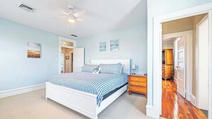 Une chambre à coucher comprenant un lit, une table de chevet, un ventilateur de plafond et une porte donnant sur une autre pièce.