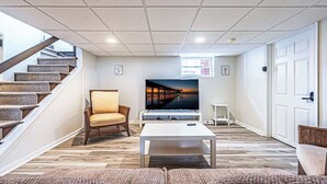 Un salon avec un téléviseur, un canapé, un fauteuil, une table basse et un escalier.